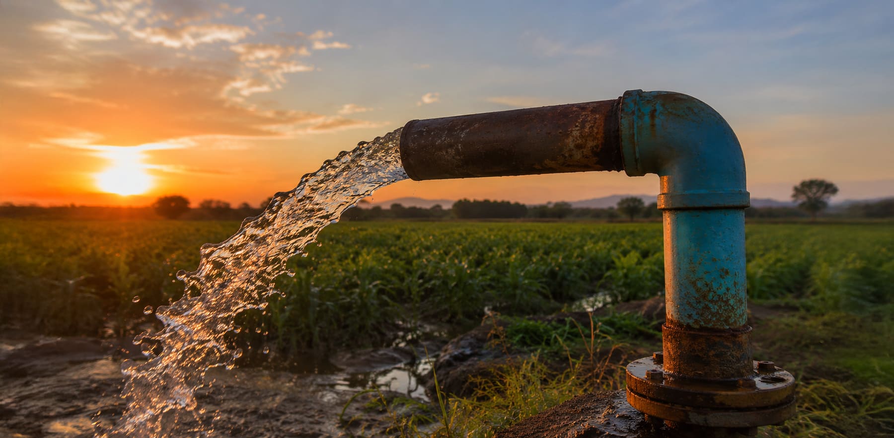 Água jorrando de um poço artesiano ao pôr do sol